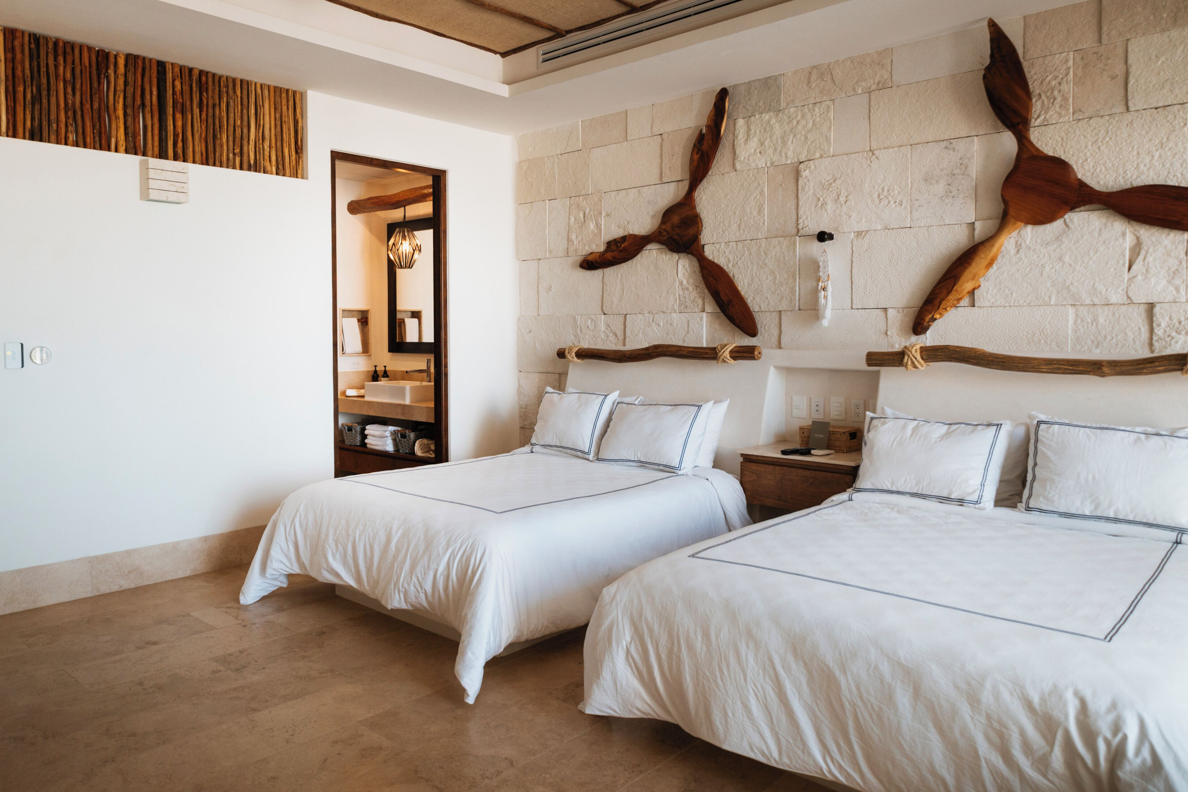 Quarto de hotel com duas camas, parede de pedra e decoração em madeira.