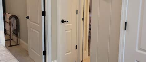 A hallway with white doors, a thermostat, and a coat rack.