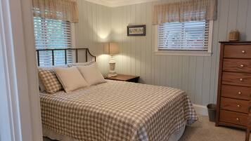 A bedroom with a bed, nightstand, lamp, dresser, and window with blinds.