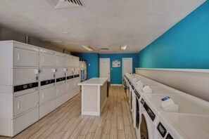 A laundry facility with multiple washing machines and dryers, a central counter, and a blue wall.
