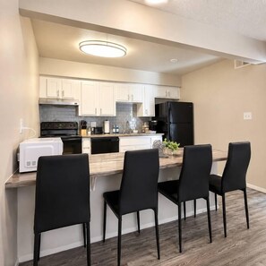 A compact kitchen with white cabinets, a black refrigerator, a microwave, and a dining area with four chairs. - Modern & Stylish Tempe 1BR | Resort Amenities (Tempe)