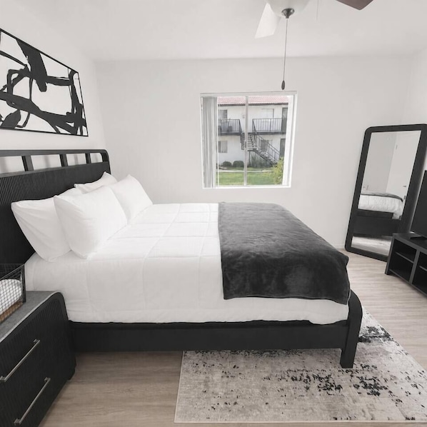 A modern bedroom with a bed, a large mirror, and a view of a building outside.