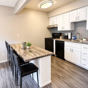 A modern kitchen with a marble countertop, black appliances, white cabinets, and a dining area with black chairs.
