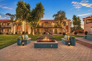 A courtyard with a fire pit, outdoor seating, and a building with balconies and string lights.
