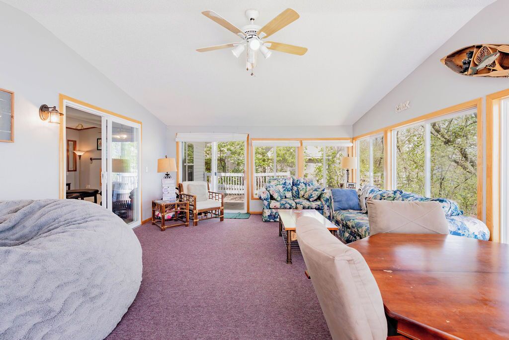 Une pièce spacieuse avec un ventilateur de plafond, un grand pouf, une table en bois et un canapé à motifs floraux.