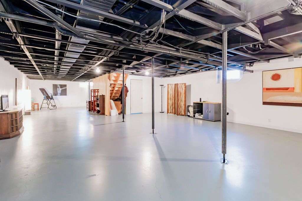 Un espacio interior con techo alto, conductos expuestos y piso de concreto pulido.