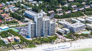 Un grand hôtel à plusieurs étages, doté d’un parking et d’un espace de plage aménagé avec des parasols.