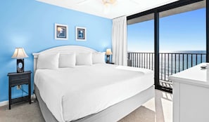Une chambre avec un grand lit, deux tables de chevet, une commode, une coiffeuse et un balcon avec vue sur la mer.