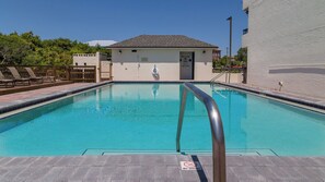 Une piscine rectangulaire avec une rambarde métallique, un panneau indiquant « INTERDIT DE PLONGER » et, au fond, un petit bâtiment doté d’un toit en tuiles.