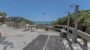 Une terrasse en bois avec des meubles d’extérieur, un mât pour drapeau et une vue sur l’océan.