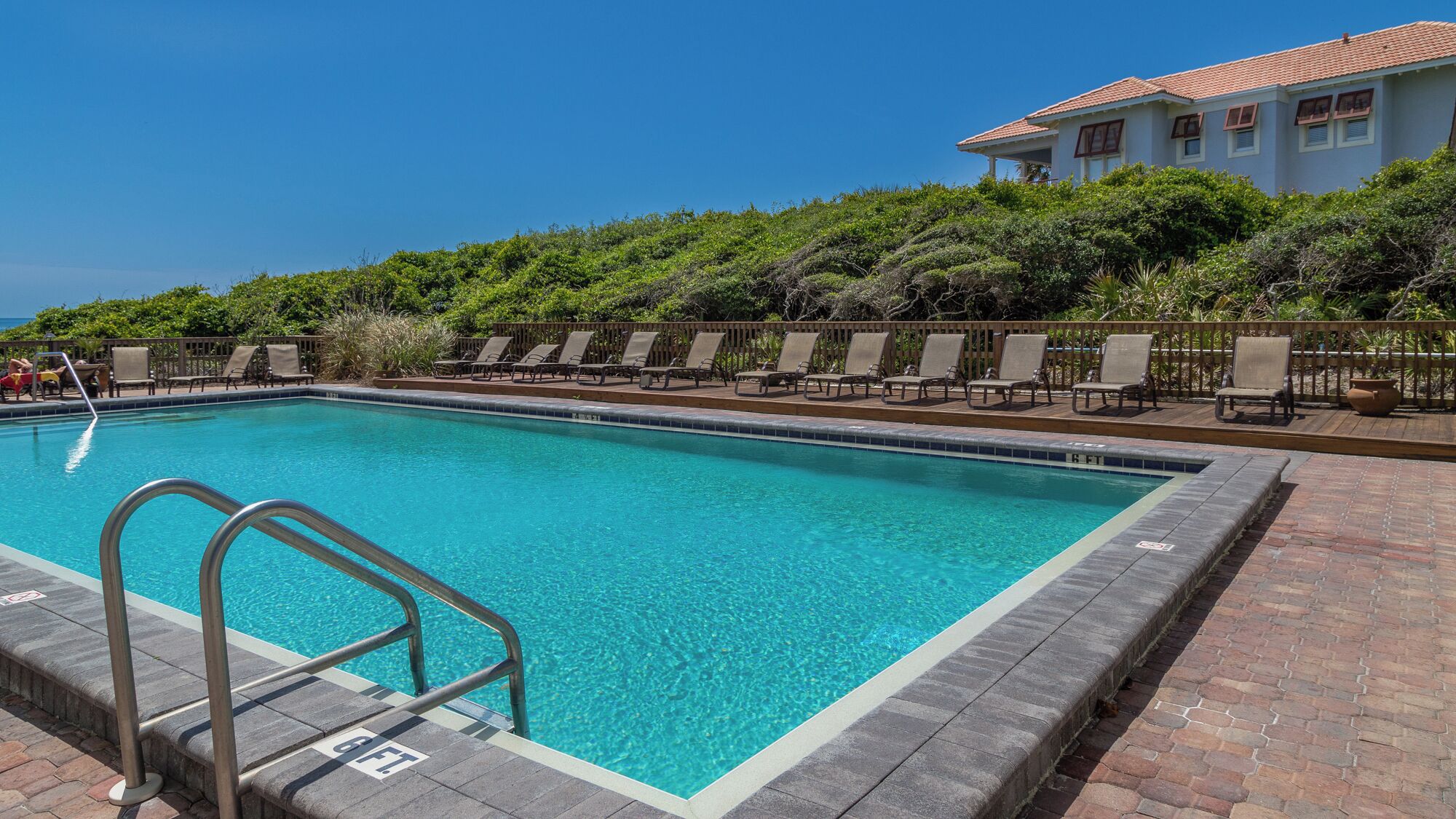 A rectangular swimming pool with clear blue water, surrounded by a brick deck and metal railings.