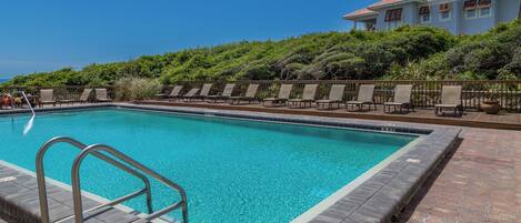 A rectangular swimming pool with clear blue water, surrounded by a brick deck and metal railings.