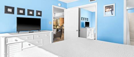 A bedroom with a large bed, a TV on a dresser, and a door leading to a bathroom.