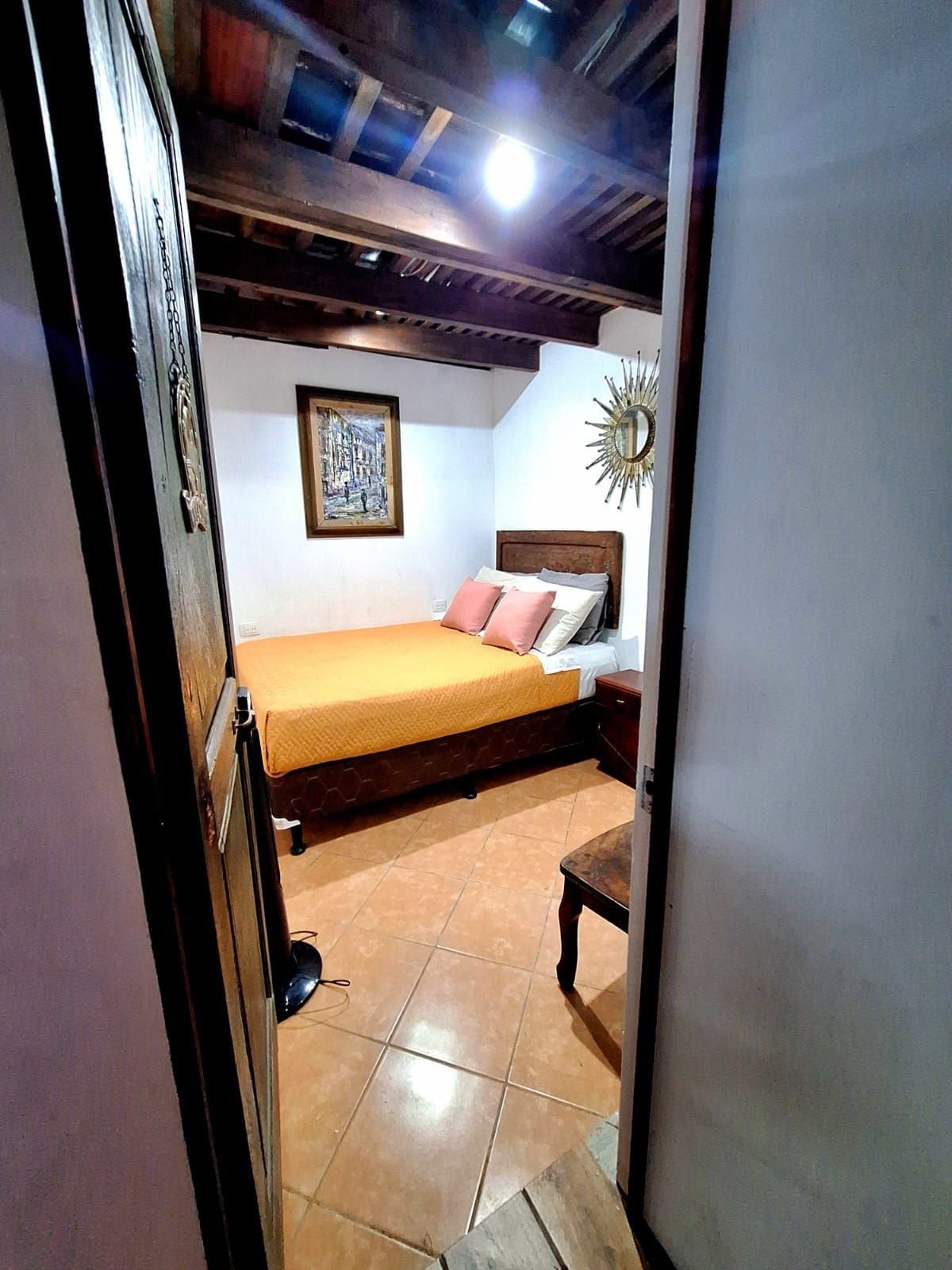 Un dormitorio con cama, mesita de noche, espejo en la pared y un cuadro enmarcado.