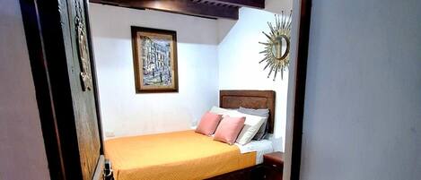 Un dormitorio con cama, mesita de noche, espejo en la pared y un cuadro enmarcado.