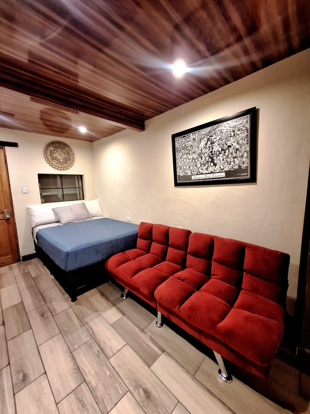 Una habitación con una cama, un sofá rojo, un cuadro en la pared y techo de madera.