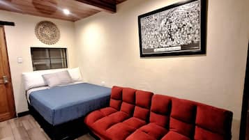 Una habitación con una cama, un sofá rojo, un cuadro en la pared y techo de madera.