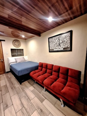 A room with a bed, a red sofa, a wall-mounted picture, and a wooden ceiling.