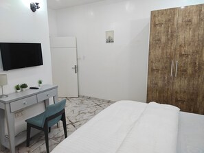 A bedroom with a bed, a desk with a chair, a television, and a wardrobe. - Lux Shortlets Hotels in Lekki Phase 1 (Lekki)