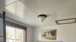 Une chambre à coucher avec un grand lit, une tête de lit ornée de boutons, un tableau représentant une grange et une fenêtre avec des stores.