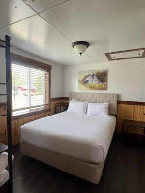 Ein Schlafzimmer mit einem großen Bett, einem knopfbesetzten Kopfteil, einem Bild von einer Scheune und einem Fenster mit Jalousien.