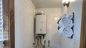 Une petite salle de bain comprenant des toilettes, un réservoir blanc, un porte-serviettes avec des serviettes, une fenêtre avec des stores et un luminaire.