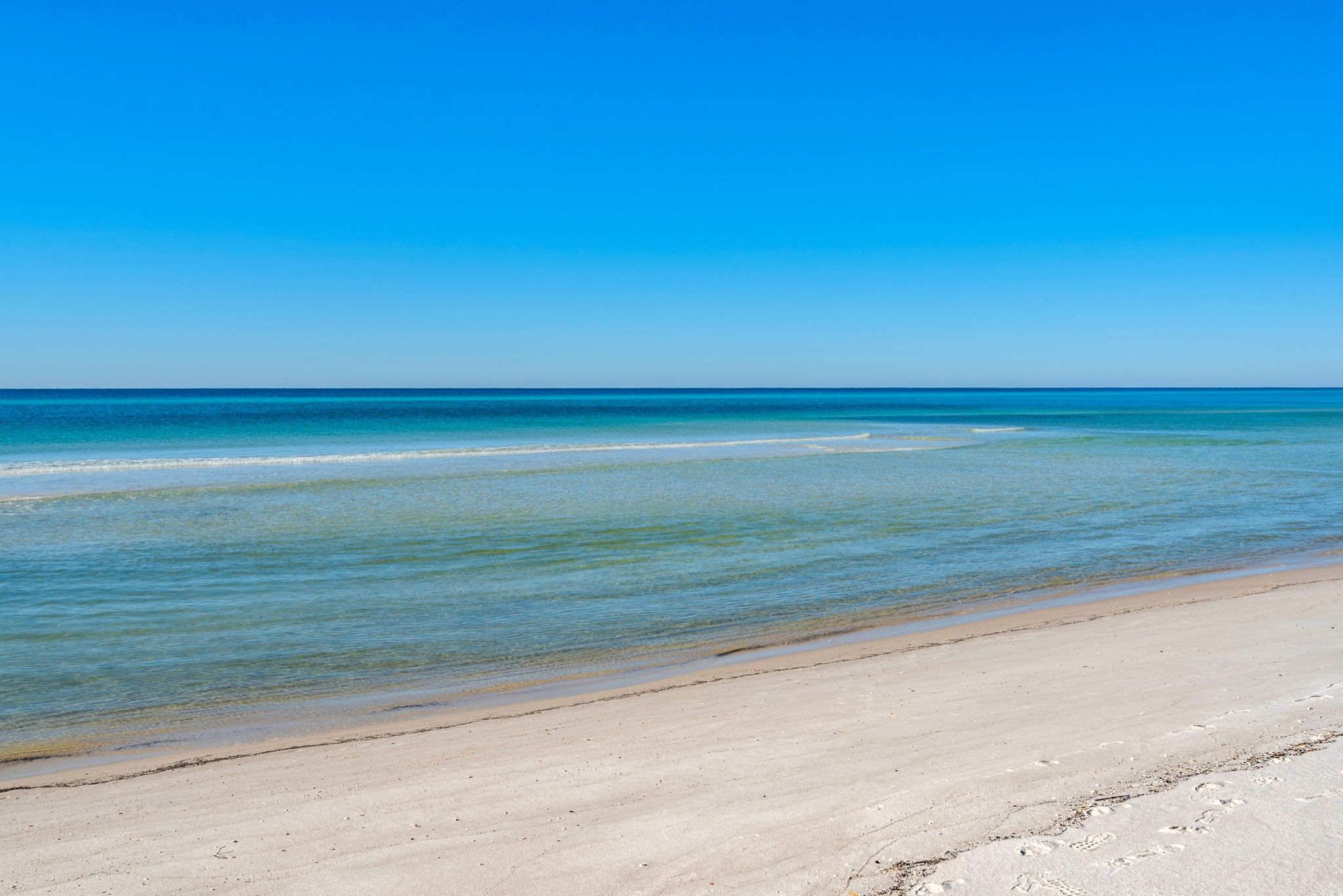 A beach with clear blue water and a sandy shore.