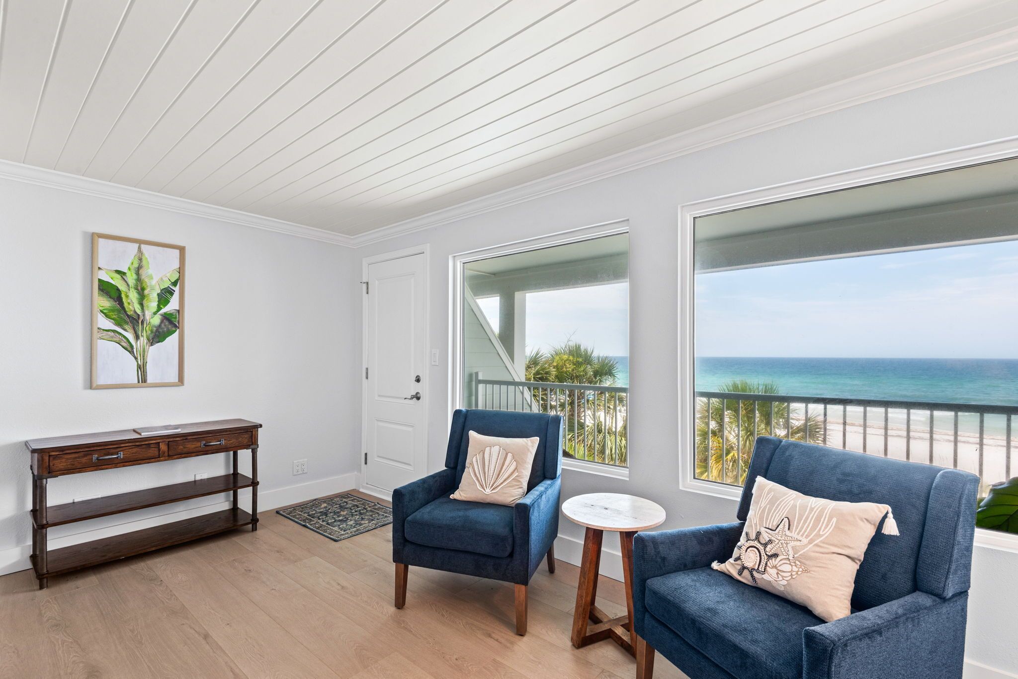 Een balkon met uitzicht op zee, twee blauwe fauteuils, een klein rond tafeltje en een houten bijzettafeltje.