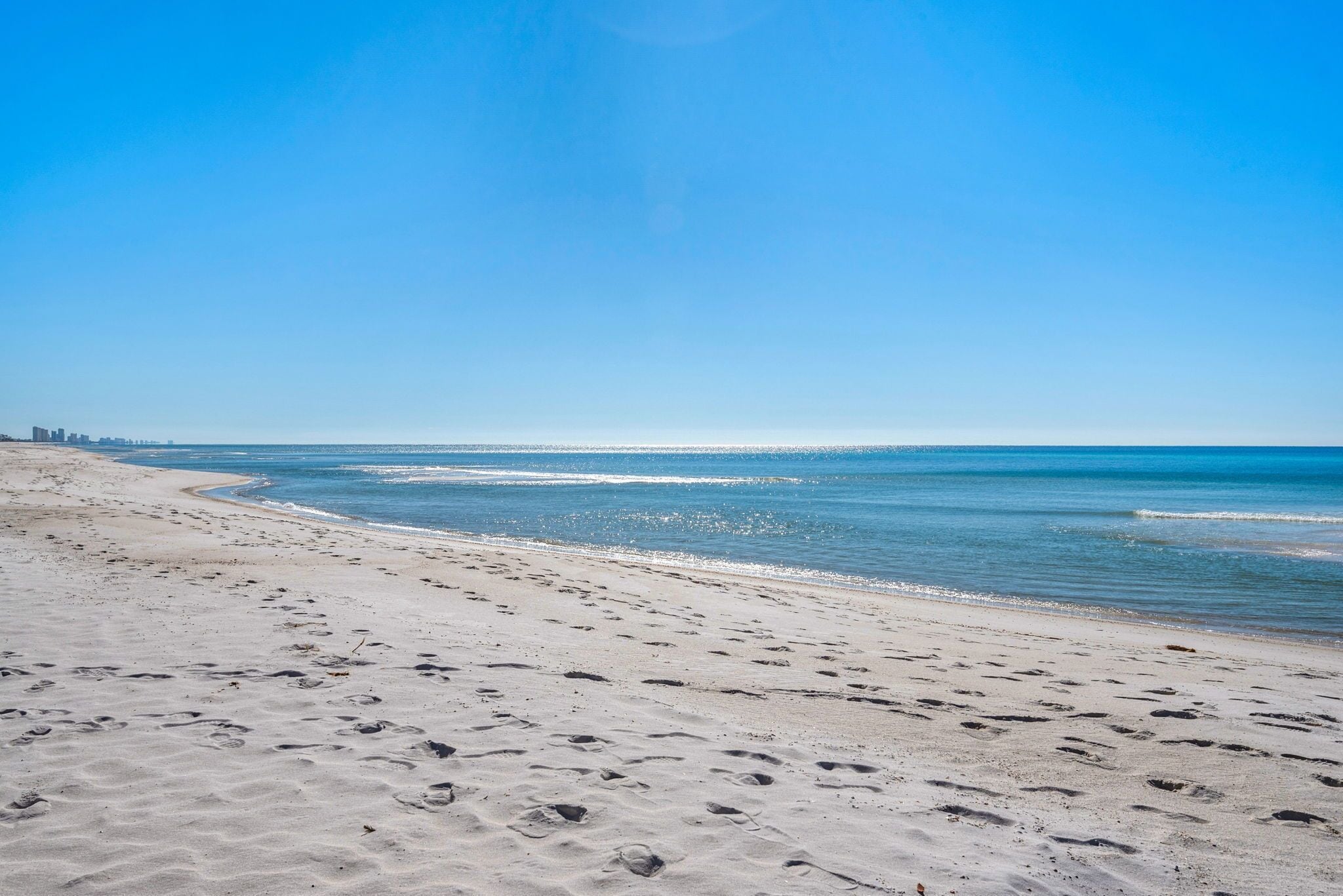 A beach with footprints, a clear sky, and a distant city skyline.