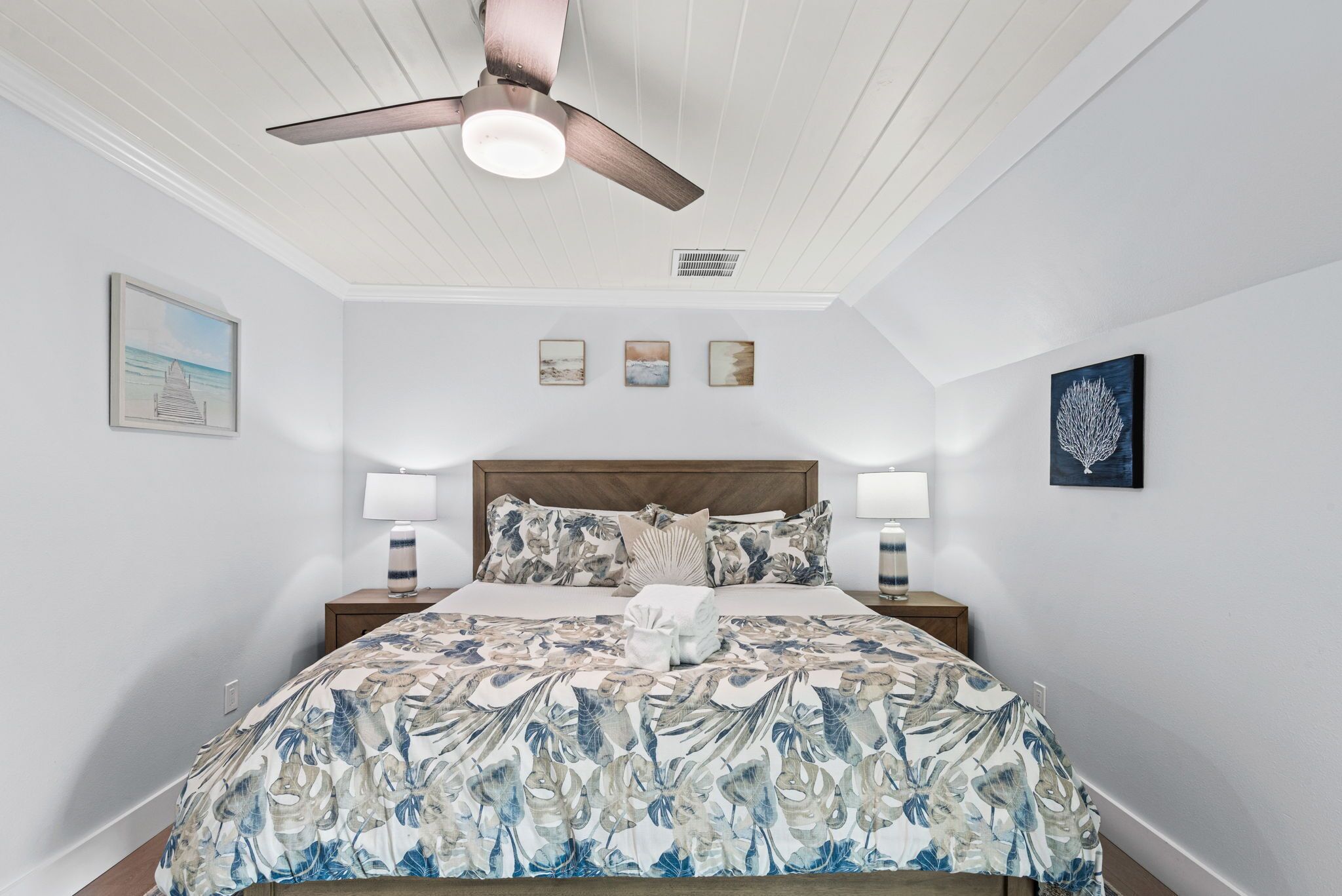 Un dormitorio con cama, dos mesitas de noche, un ventilador de techo y decoración en la pared.