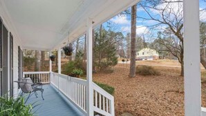 A covered porch with a railing, a table, and chairs.
