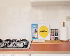 Een keukenblad met een gasfornuis, een kookboek, een deegroller en zoutstrooiers.