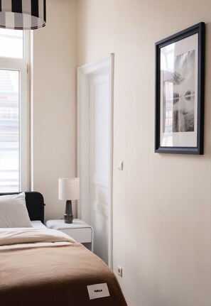 A hotel room with a bed, a nightstand, a lamp, a framed picture on the wall, and a door. - Bright & Modern 2 Bedroom Apartment in Ixelles (Ixelles)