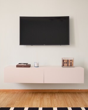 Een flatscreen televisie bevestigd aan een muur boven een minimalistische witte console met enkele objecten erop.