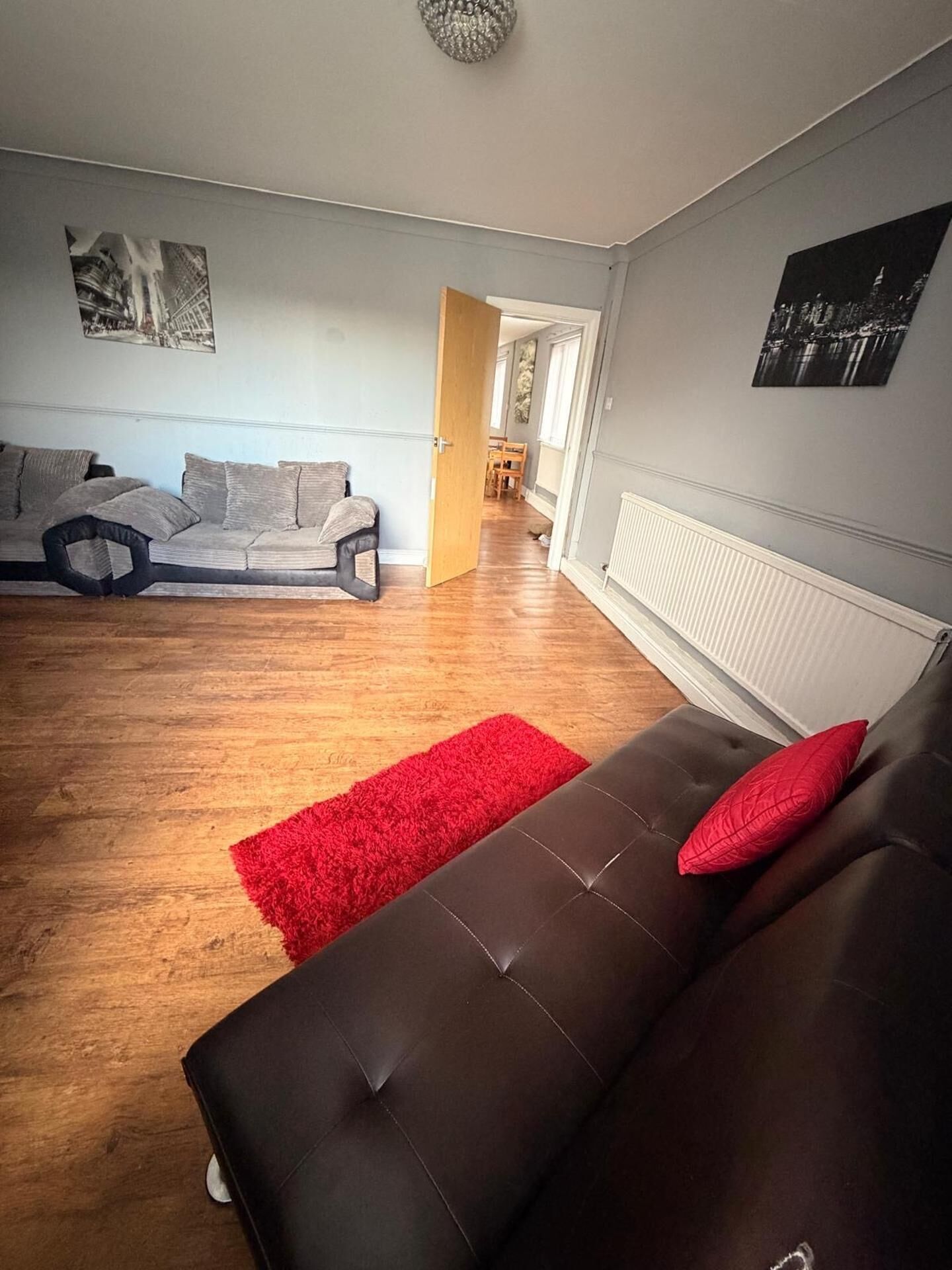 A living room with a brown sofa, a red rug, and a cityscape painting on the wall.