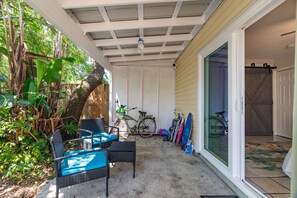 A covered patio area with outdoor furniture, a bicycle, and a sliding glass door leading to an interior space. - Pier Escape A - WiFi, AC, Close to Beach (Jacksonville Beach)