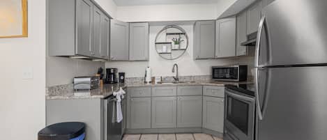A compact kitchen with grey cabinets, a stainless steel refrigerator, a microwave, a toaster, and a coffee maker.