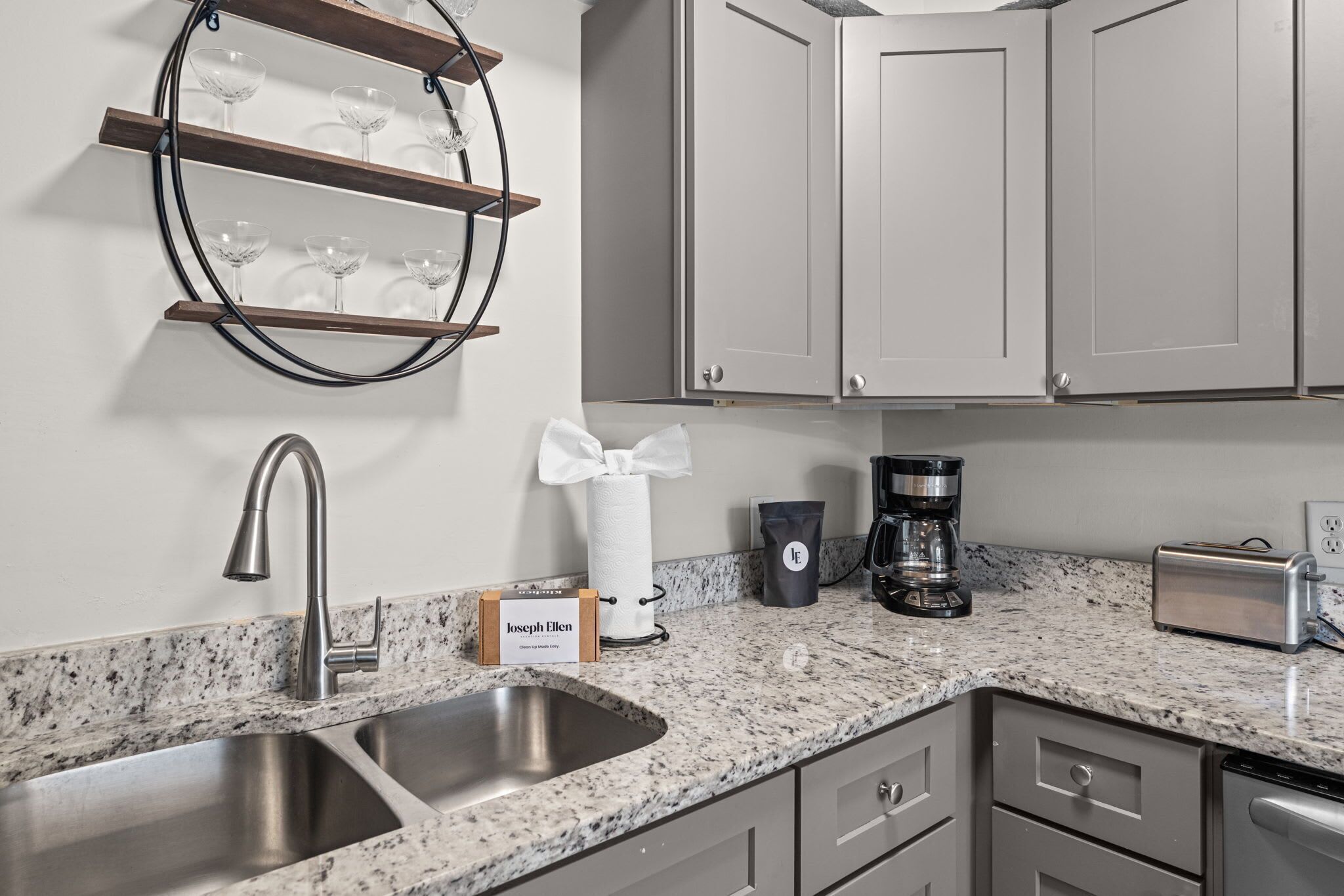 A kitchen with a granite countertop, stainless steel sink, and a coffee maker.
