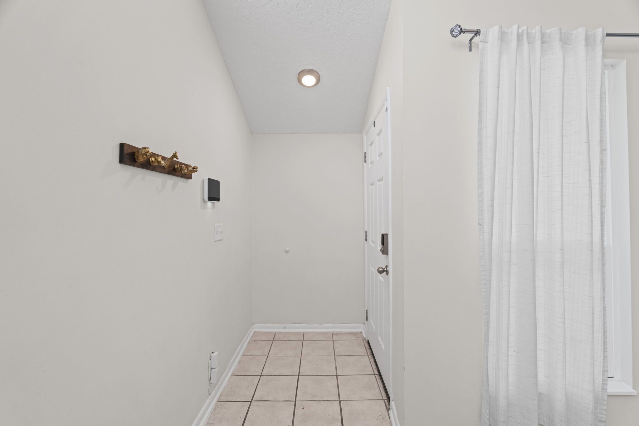 A narrow hallway with a tiled floor, a white door, and a shower curtain.