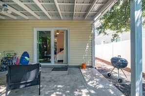 A covered patio with a grill, a chair, and a surfboard. - Pier Escape - Entire Property (Jacksonville Beach)