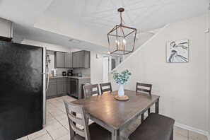 Une cuisine moderne avec un coin repas, comprenant un réfrigérateur noir, des armoires grises et un luminaire suspendu.