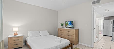 A bedroom with a bed, bedside table, lamp, dresser, and a ceiling fan.