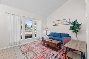 Ein Wohnzimmer mit einem blauen Sofa, einem Couchtisch, einem Teppich und einer Pflanze.