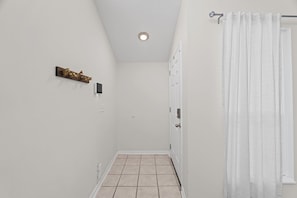 A narrow hallway with a tiled floor, a white door, a white curtain, and a ceiling light fixture. - Pier Escape B - WiFi, AC, Close to Beach (Jacksonville Beach)