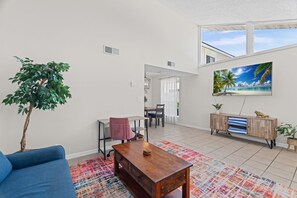 A modern living room with a blue sofa, a wooden coffee table, and a dining area with a table and chairs. - Pier Escape B - WiFi, AC, Close to Beach (Jacksonville Beach)