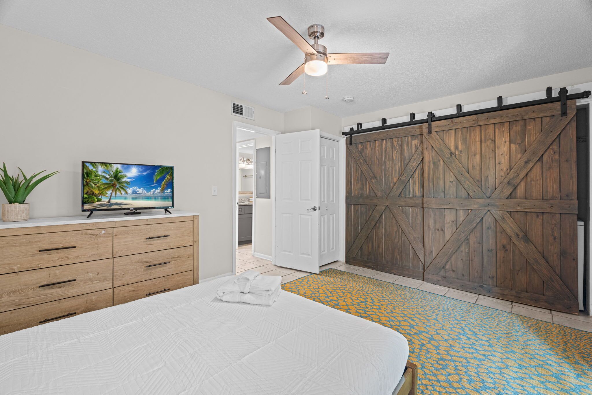 A bedroom with a bed, a dresser, a television, a ceiling fan, and a wooden barn-style door.