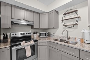 A modern kitchen with grey cabinets, stainless steel appliances, a granite countertop, and a wine rack. - Pier Escape B - WiFi, AC, Close to Beach (Jacksonville Beach)