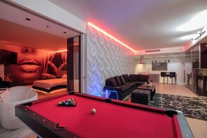 A modern living room with a pool table, a sofa, and a large wall mural. - Remodeled Corner Suite - Wraparound Balcony & Panoramic Strip Views (Las Vegas)