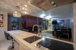 A modern kitchen with a central island, a dining area with a table and chairs, and a living room with a TV and seating. - Remodeled Corner Suite - Wraparound Balcony & Panoramic Strip Views (Las Vegas)