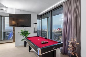 Une chambre moderne équipée d’une table de billard, d’un téléviseur à écran plat et d’une grande fenêtre donnant sur la ville.